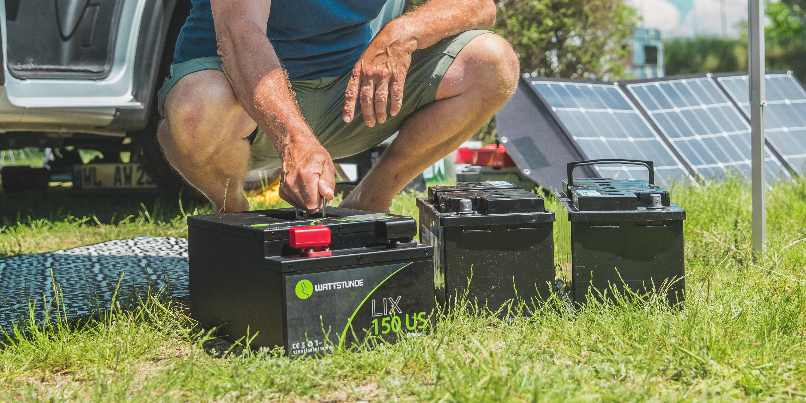 Ein Mann schließt eine AGM-Batterie an einer Solartasche an. Daneben noch zwei weitere Batterien und eine Solartasche.