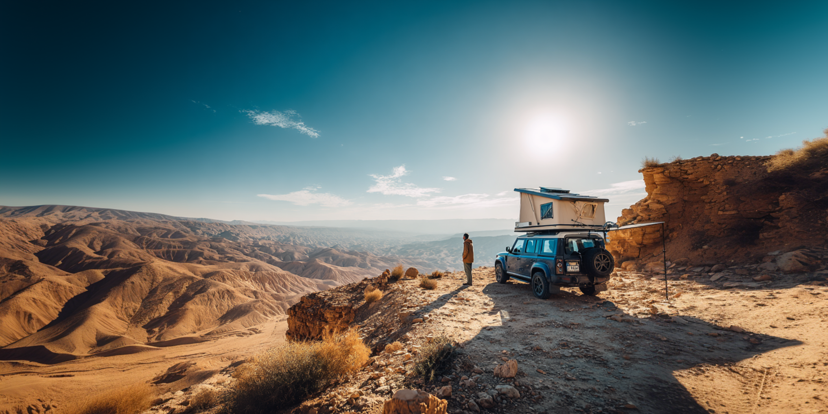Ein Blick durch die Berglandschaft: Die Sonne scheint, der Himmel ist blau - im Hintergrund ein Geländewagen mit Dachzelt und flexible Solarmodule.