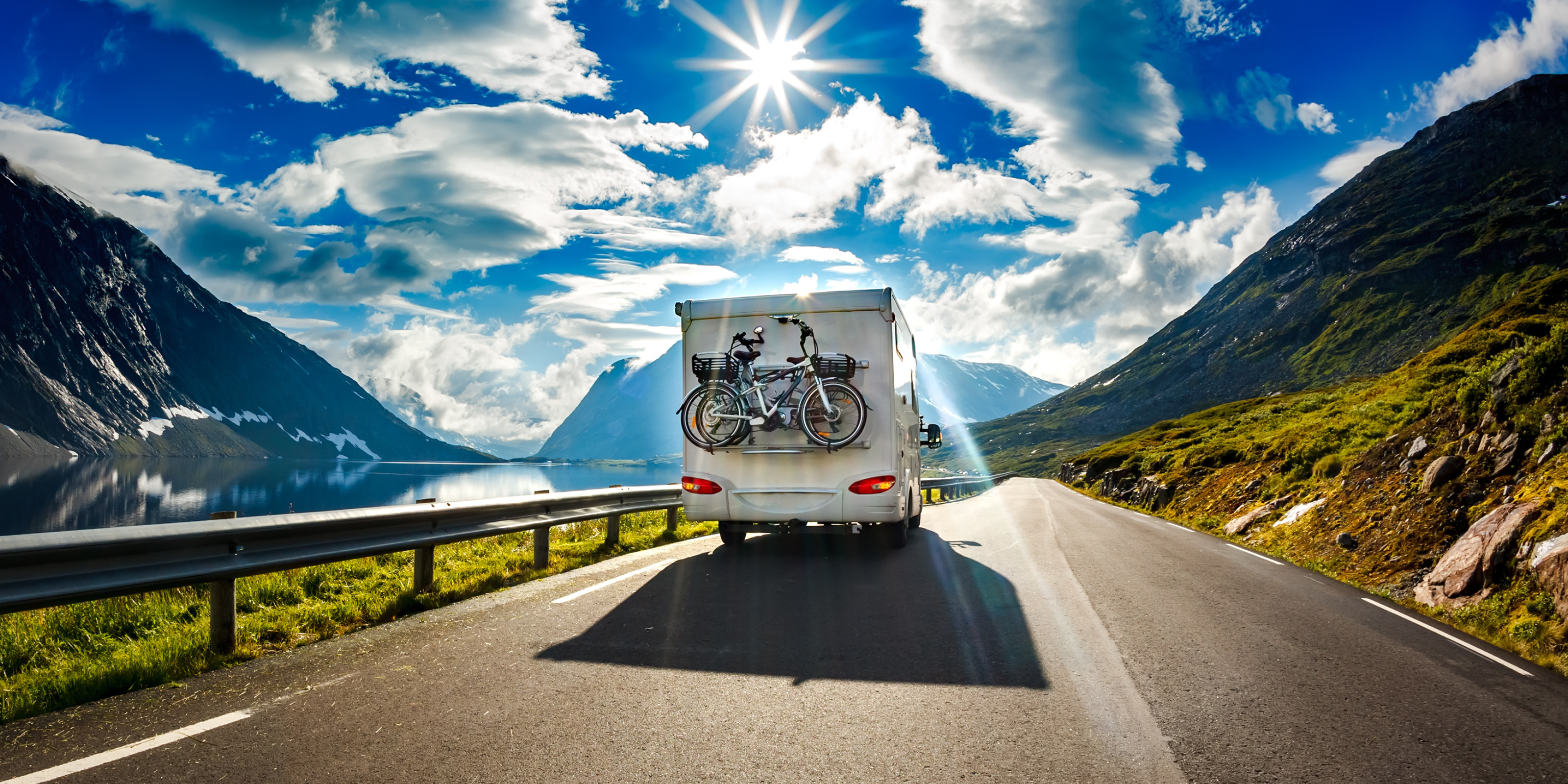 Ein Wohnmobil "on the road" - ausgestattet mit Fahrradträger und Solaranlage - im Hintergrund Sonne und blauer Himmel.