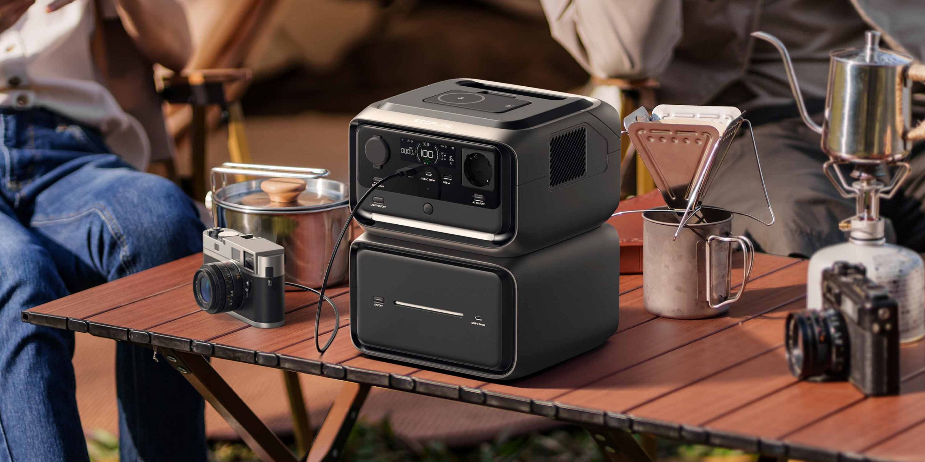 Auf einem Tisch steht eine Kamera eine Powerstation von EcoFlow, eine Tasse und ein Gaskocher mit einer Kaffeekanne.