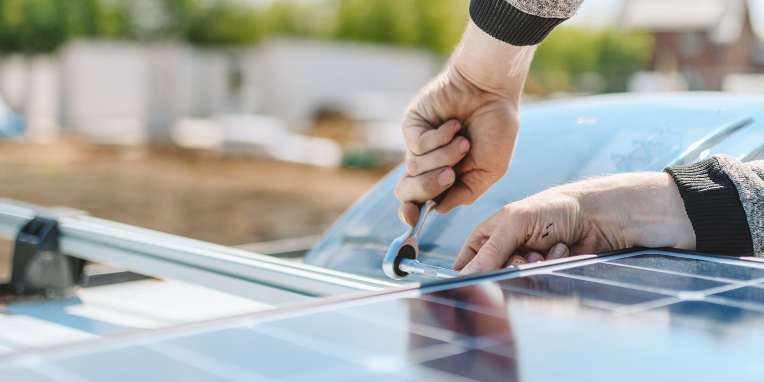 Eine Person schraubt auf dem Dach eines Reisefahrzeuges ein Solarmodul an einer Halterung fest.