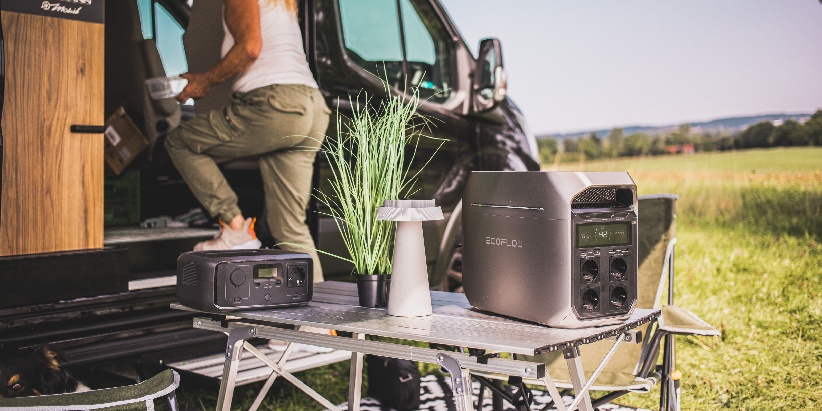 Vor einem Camper steht ein Tisch auf dem zwei Powerstation von EcoFlow stehen. Eine Frau geht gerade in den Camper.