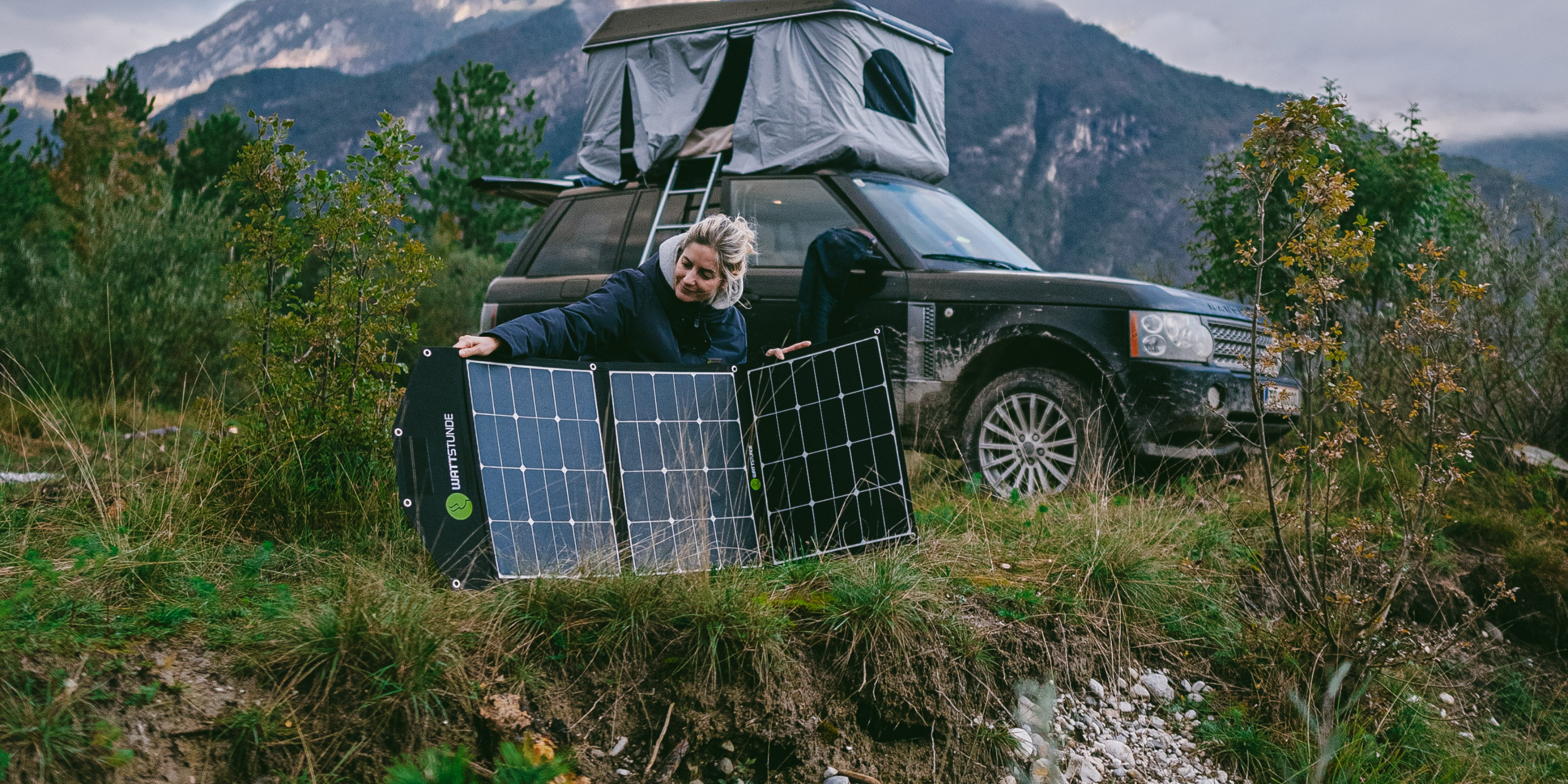 Eine Frau stellt die SOLA Ease Solartasche von WATTSTUNDE auf, hinter hier ist ihr Reisefahrzeug.