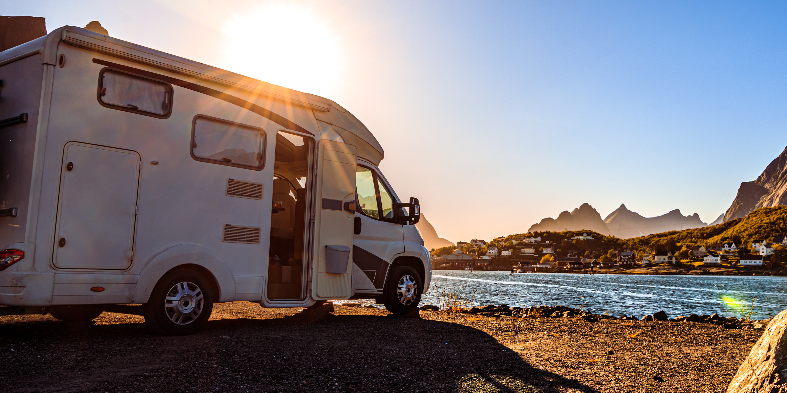 Ein Wohnmobil, bestückt mit einer Solaranlage, am Ufer eines Flusses beim Sonnenuntergang.