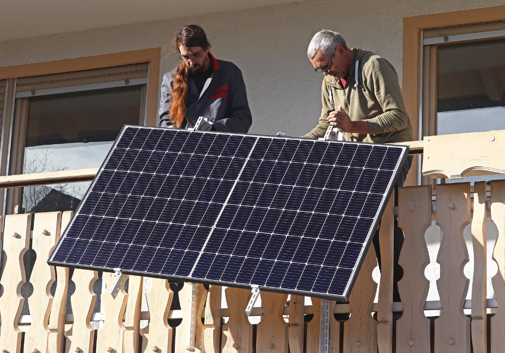 Solarmodul wird von zwei Personen an die Balkonfassade angebracht